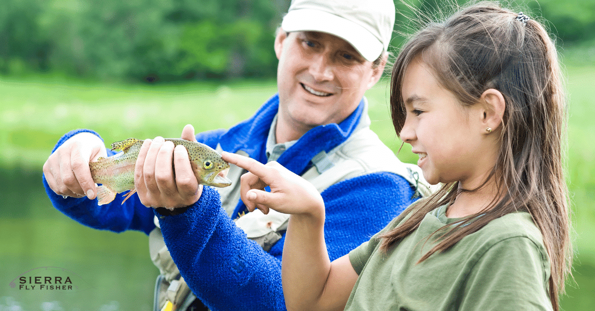 A man and a young girl proudly hold a fish, showcasing their successful fly fishing experience together.