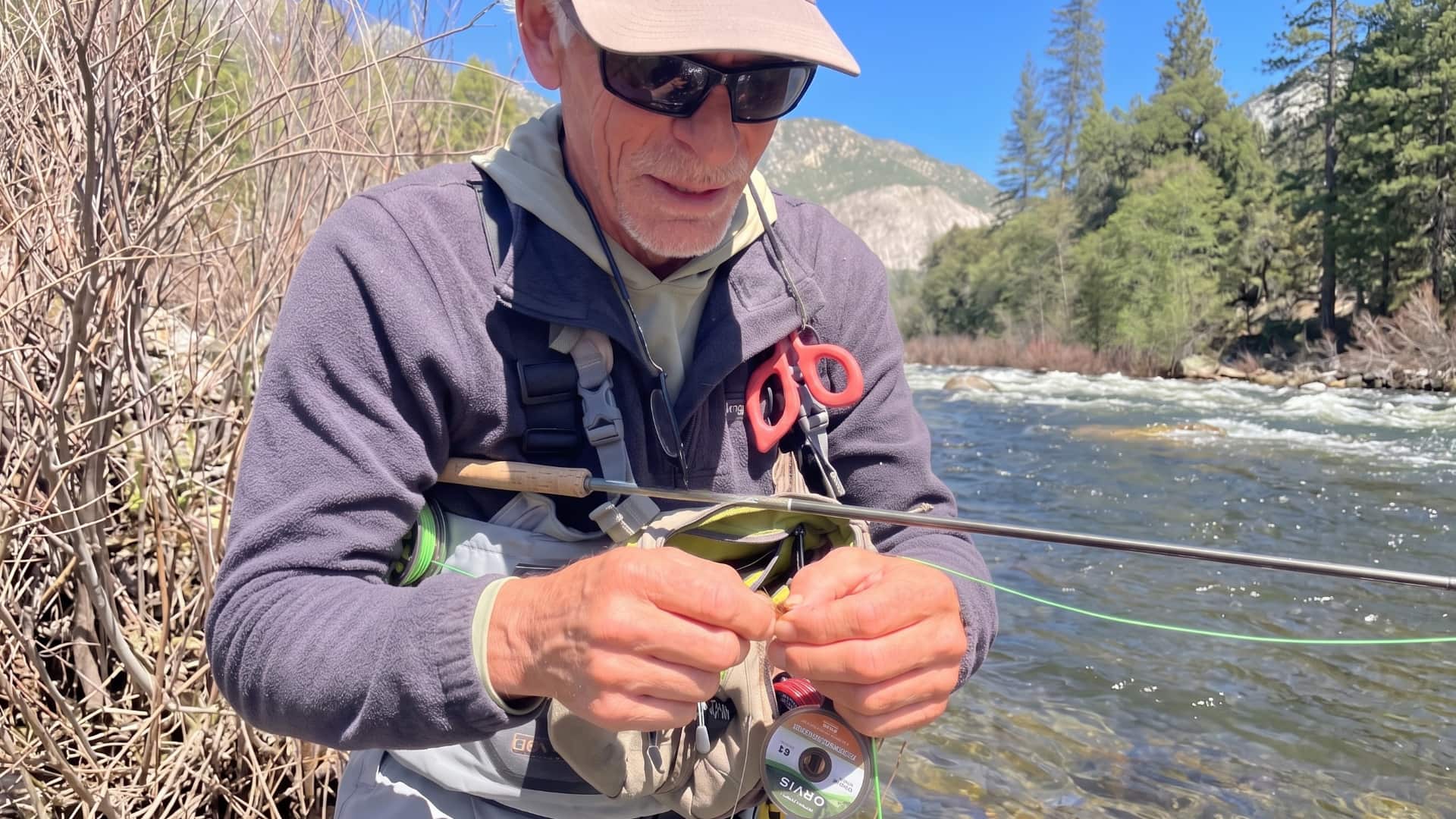 Angler tying a fly fishing knot on tippet beside a High Sierra river